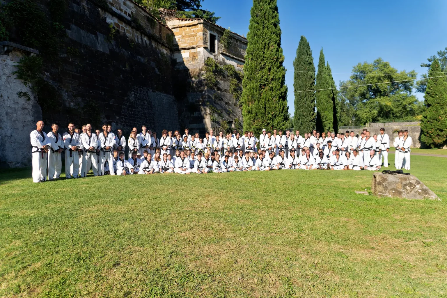 Große Gruppe von Taekwondo-Sportlern in Doboks für ein Teamfoto vor einer historischen Steinmauer.