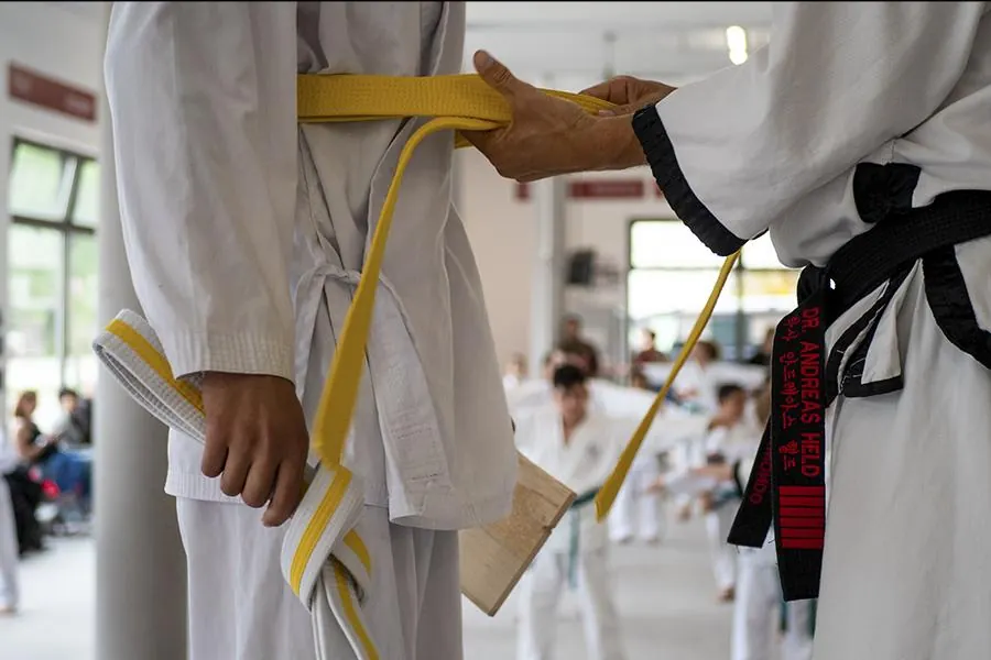 Taekwondo Gürtelprüfung: Ein Meister der einen Schüler den Gürtel fesbindet