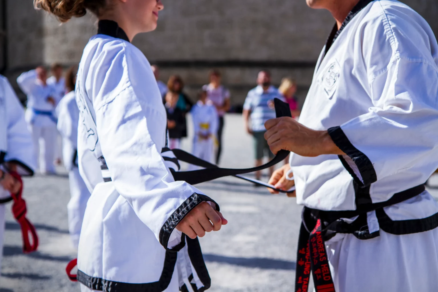 Nahaufnahme einer Gürtelprüfung, bei der ein Taekwondo-Meister einer Schülerin den schwarzen Gürtel bindet.