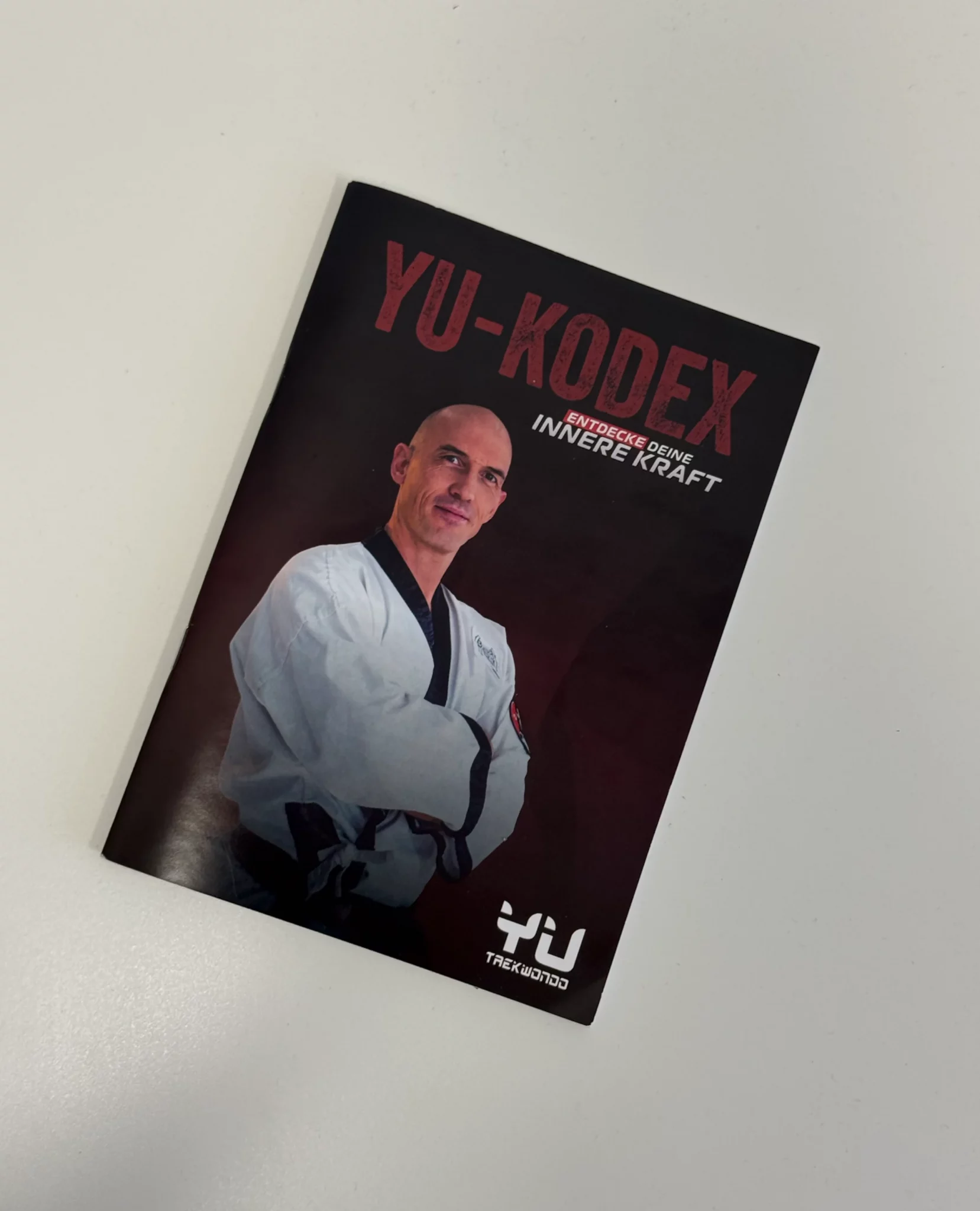 Yu-Kodex Broschüre mit dem Titel „Entdecke deine innere Kraft“ und Porträt eines Taekwondo-Meisters.
